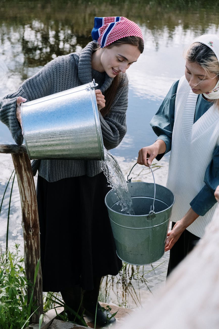 women standing by a body of water and pouring water from bucket to bucket